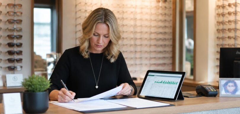 Optician reviewing bookkeeping records and financial charts at practice reception desk