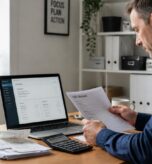 Business owner reviewing a VAT return and receipts at a desk with a laptop showing financial figures